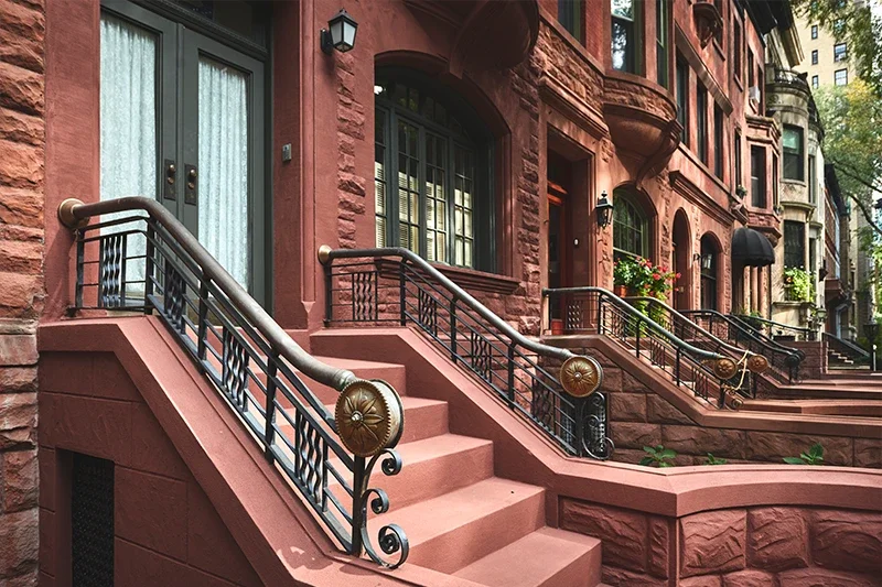 Row of brownstone townhouses with front stairs and ornate black metal railings extending towards the street.