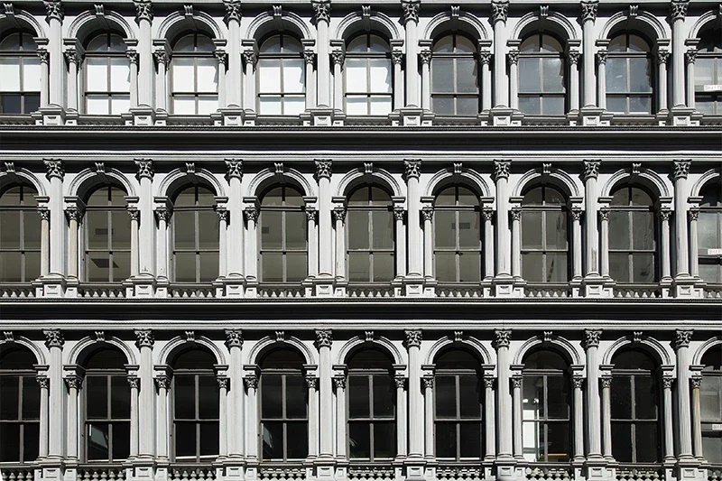 A gray building facade with three rows of arched windows, each framed by decorative columns and moldings.