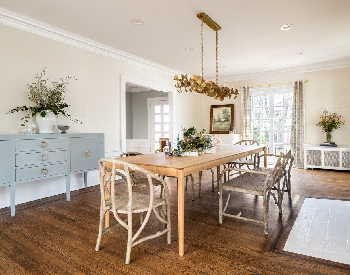 A spacious dining room features a wooden table, chairs, and a decorative chandelier with natural light streaming through windows.