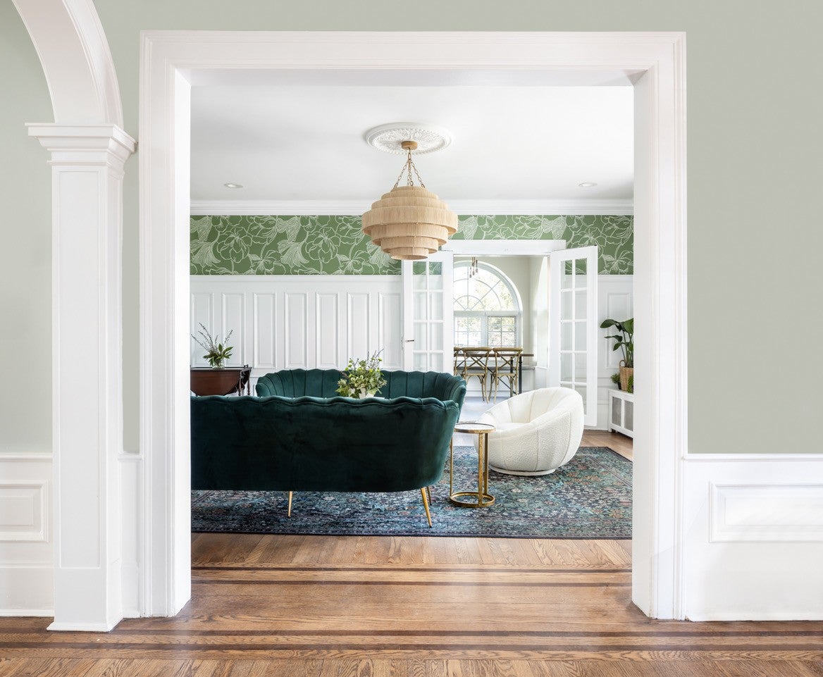 A green velvet sofa and armchair sit on a patterned rug in an elegant living room decorated with wallpaper.