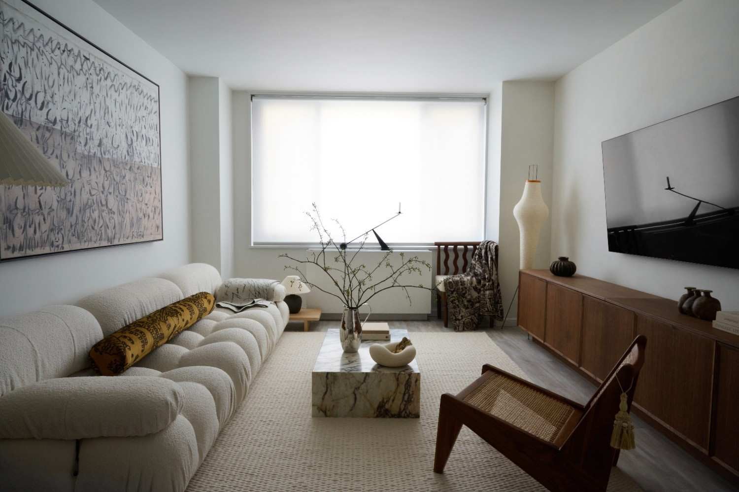 A modern living room with a cream-colored, tufted sofa, marble coffee table, and wood and cane chair.