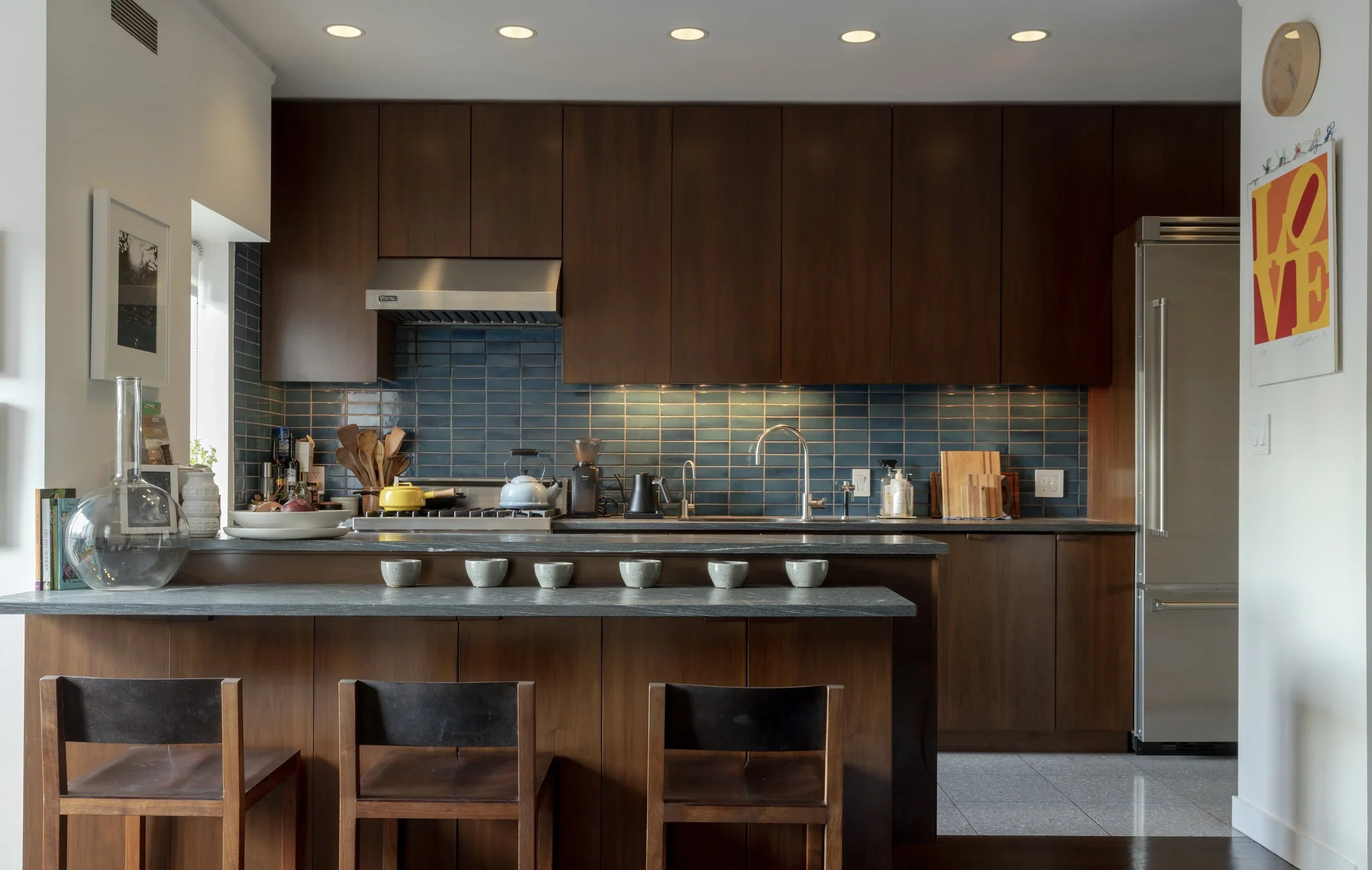 A modern kitchen with white cabinets, a white island, stainless steel sink, wood floor, and a white door partially open.