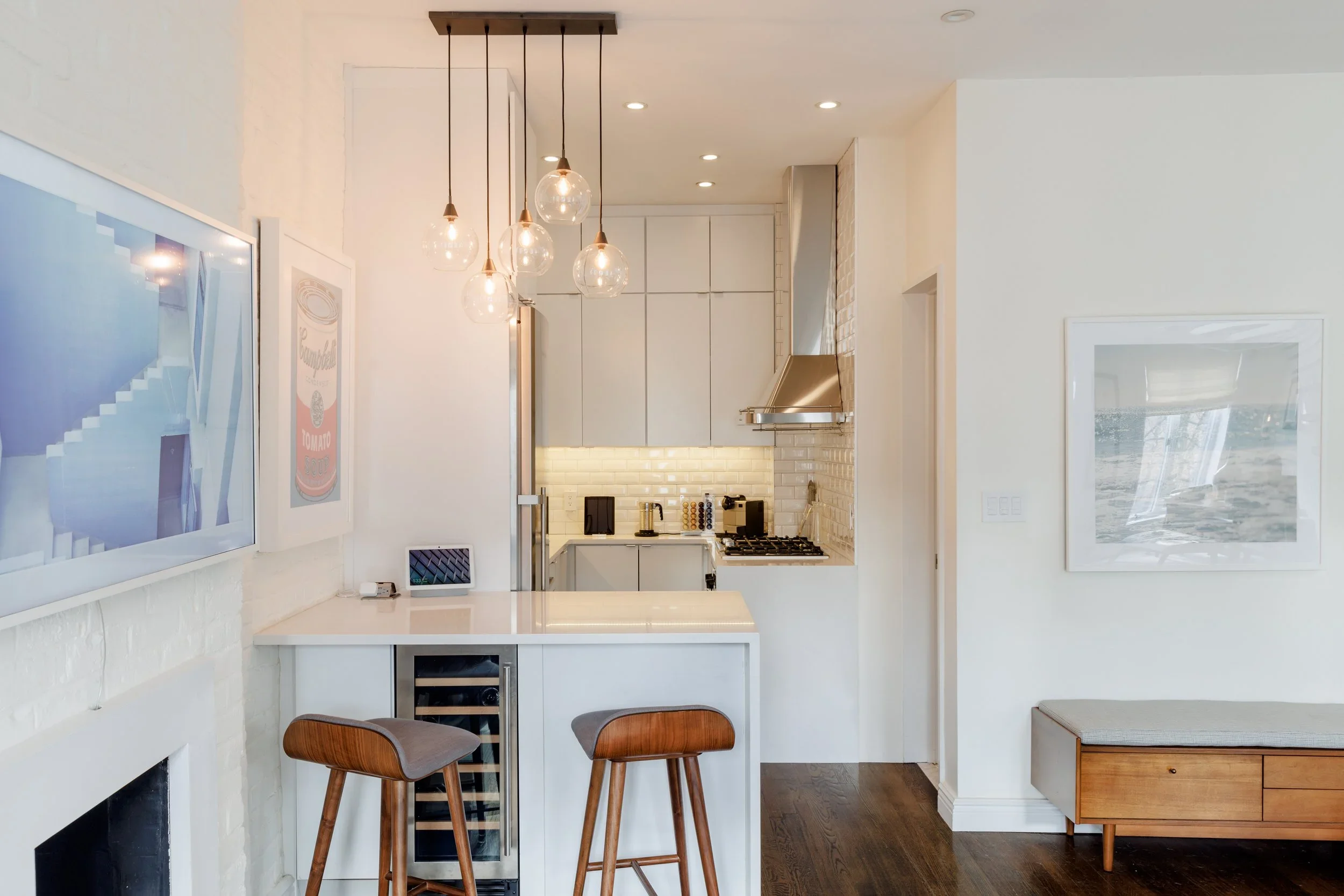 Bright, modern apartment interior with white walls, a compact kitchen, and a living area featuring a TV over a fireplace.